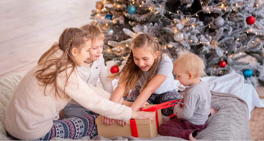 Kids opening a gift in the family room next to a Christmas tree.